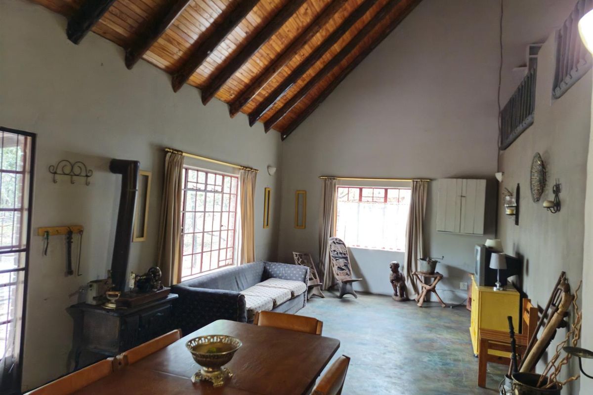 Spacious living area featuring a high vaulted timber-beamed ceiling, large windows, and a built-in fireplace, creating a rustic and open atmosphere.