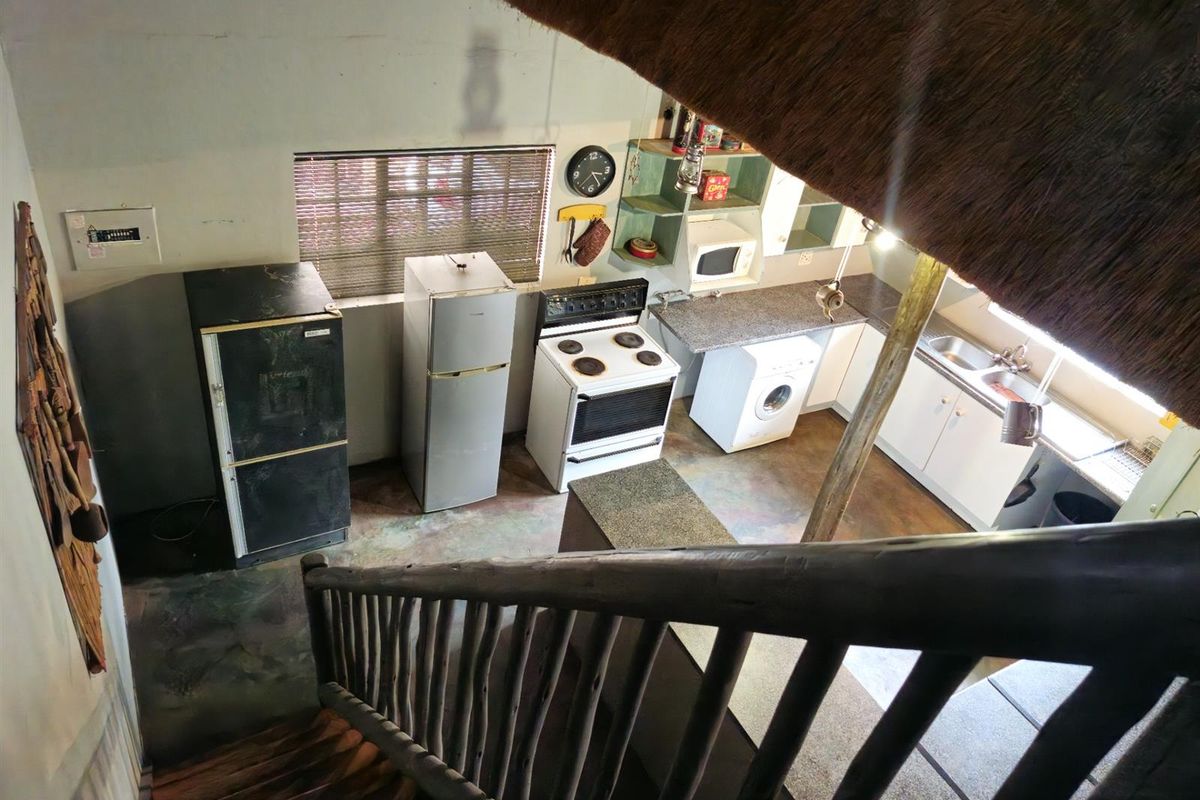 A rustic kitchen area viewed from a staircase, featuring built-in cabinetry, a freestanding stove, and a thatched roof ceiling.