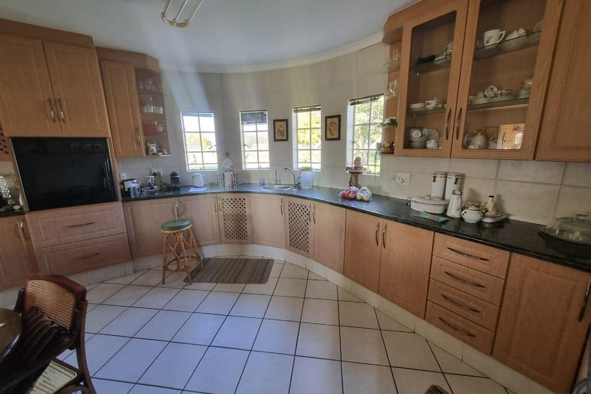 A spacious kitchen featuring curved wooden cabinetry, dark countertops, integrated oven, and tiled flooring with natural light from multiple windows.
