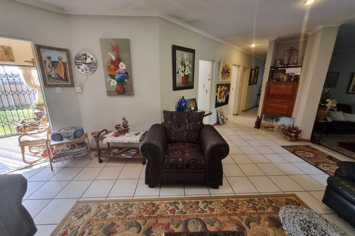 A spacious living area featuring neutral tiled flooring, recessed lighting, and a seamless transition to an adjacent hallway and outdoor access.