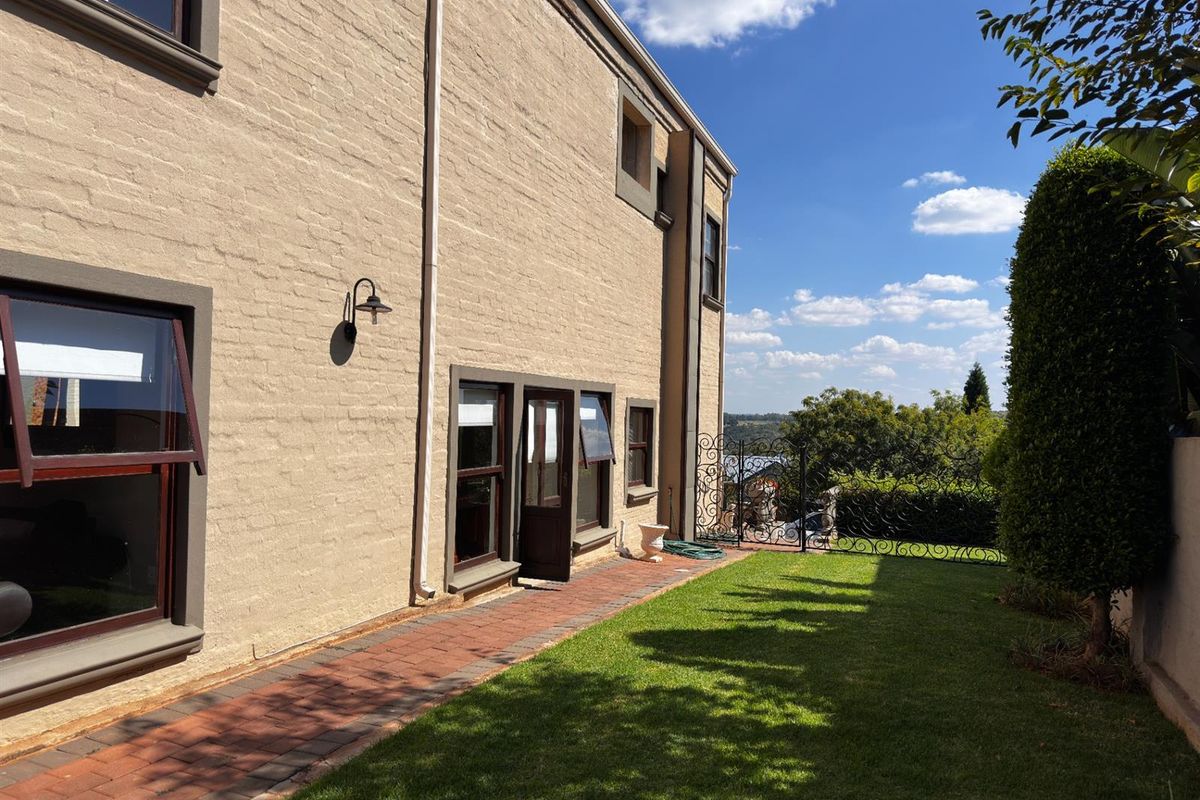 A view of the rear exterior of the house, featuring a brick pathway, manicured lawn, and decorative wrought iron fencing overlooking the landscape.