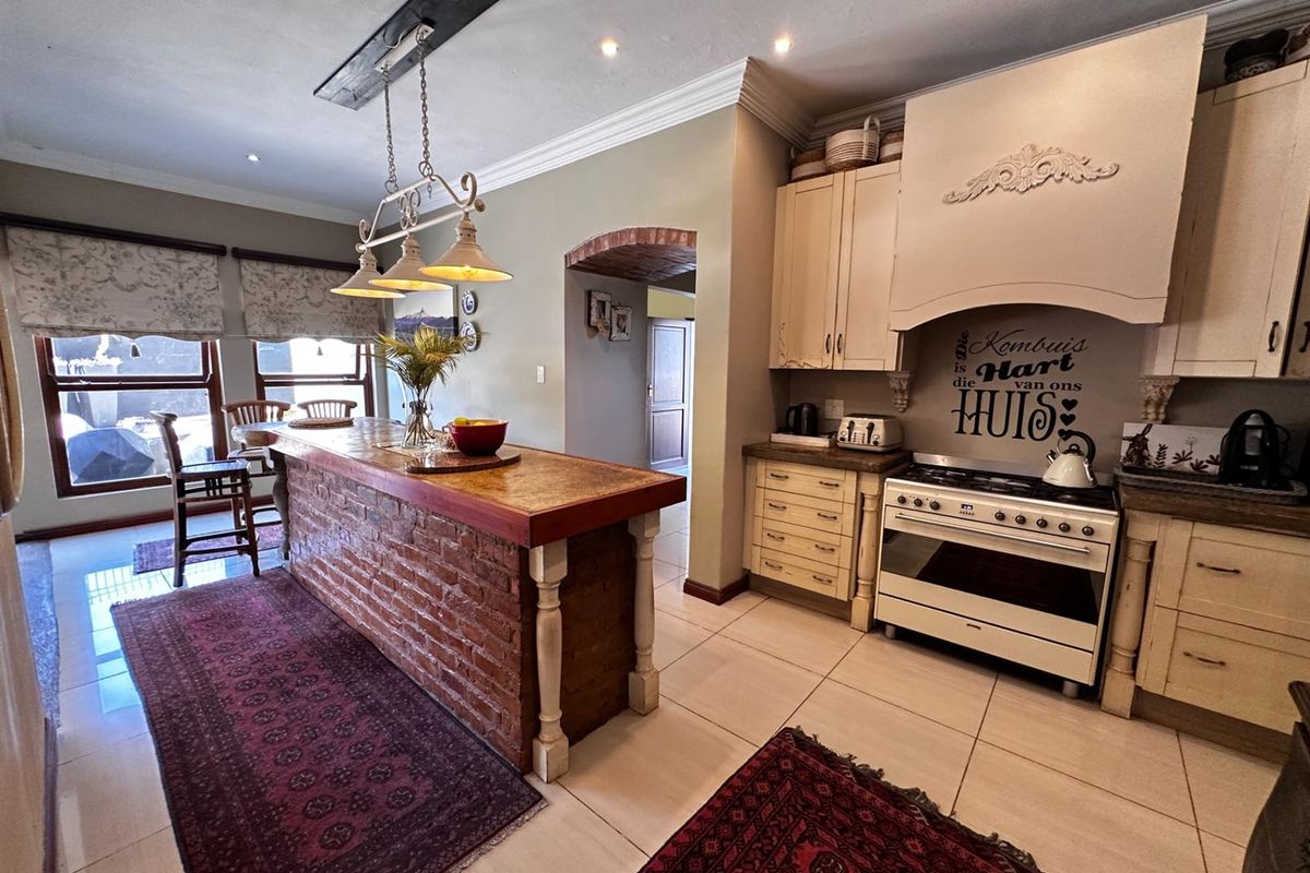 A rustic-style kitchen featuring a large brick-based island, built-in cabinetry, a gas stove with an extractor hood, and tiled flooring.