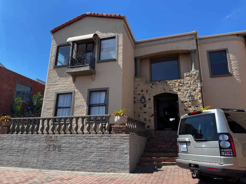 A multi-story residential facade featuring stone cladding, a balcony with wrought iron railing, and a raised terrace with a balustrade.