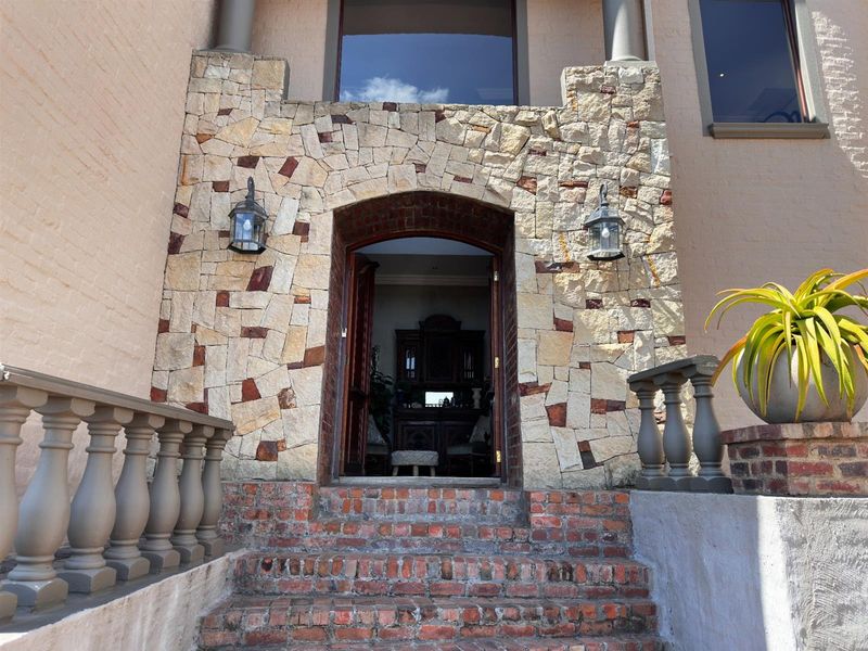 Grand entrance featuring a rustic stone-clad archway, brick staircase, and classic balustrades leading into the home.