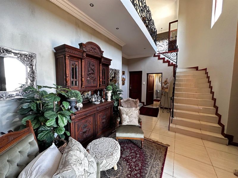 Spacious grand entrance hall featuring a tiled floor, an elegant staircase with ornate wrought iron balustrades, and a high ceiling with recessed lighting.