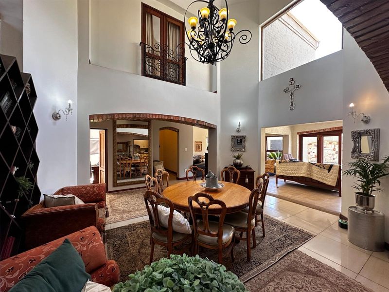 Spacious open-plan dining area featuring double-volume ceilings, a decorative wrought iron chandelier, arched brick detailing, and a mezzanine-level balcony overlooking the space.