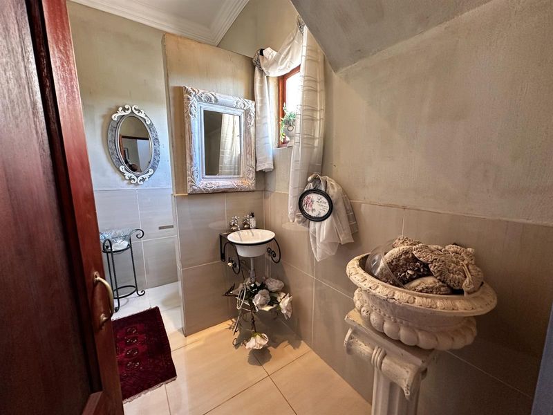 A compact bathroom featuring a pedestal sink, tiled flooring, and wall tiling, with decorative mirrors and classic architectural details.