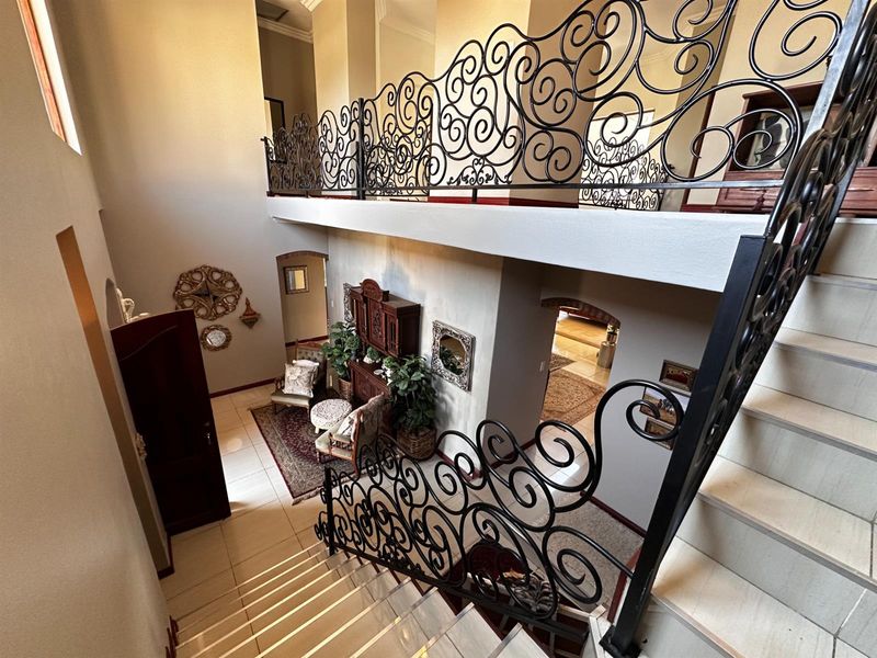 A grand double-volume entrance hall featuring a tiled staircase with ornate wrought iron balustrades and a mezzanine landing overlooking the lower level.