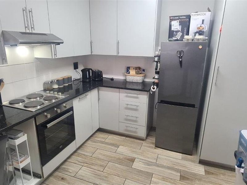 A functional kitchen featuring granite countertops, built-in cabinetry, an electric hob, and an integrated oven with a modern tiled floor finish.