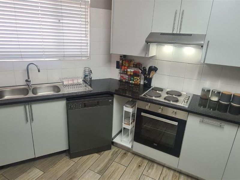 A functional kitchen featuring white cabinetry, granite countertops, a built-in oven with hob, extractor fan, and a double basin sink with tiled flooring.