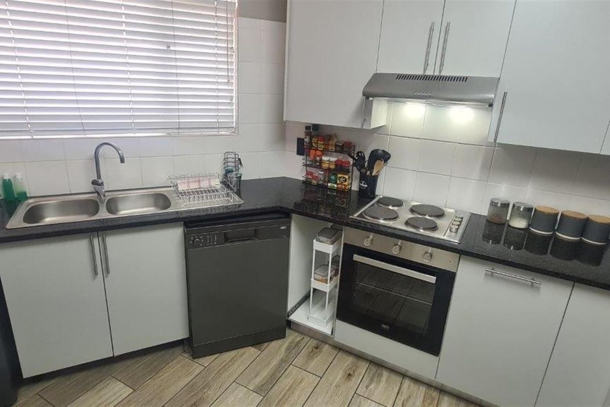 A functional kitchen featuring white cabinetry, granite countertops, a built-in oven with hob, extractor fan, and a double basin sink with tiled flooring.
