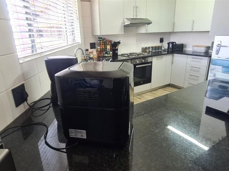 A functional kitchen featuring granite countertops, built-in cabinetry, a gas hob with extractor fan, and a tiled backsplash.