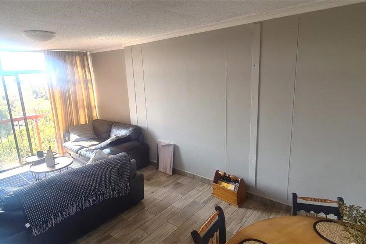 A spacious living area featuring tiled flooring and a large sliding glass door that provides access to the balcony and natural light.