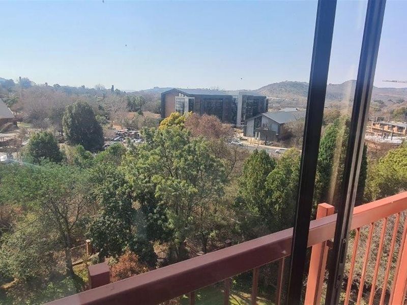 Elevated view overlooking surrounding trees, neighborhood buildings, and landscape, captured from a balcony with a metal railing.