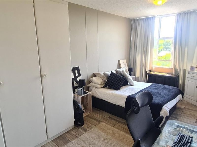 A functional bedroom featuring built-in cupboards, tiled flooring, and large windows that provide ample natural light.