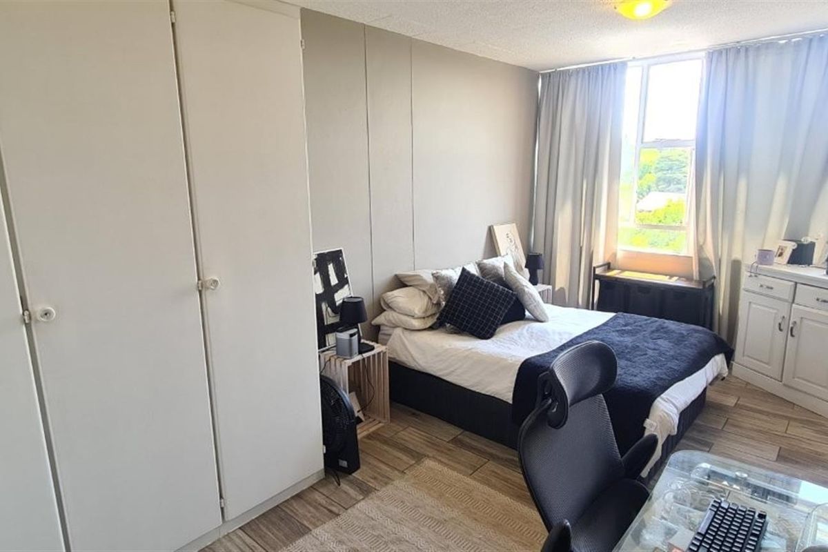 A functional bedroom featuring built-in cupboards, tiled flooring, and large windows that provide ample natural light.