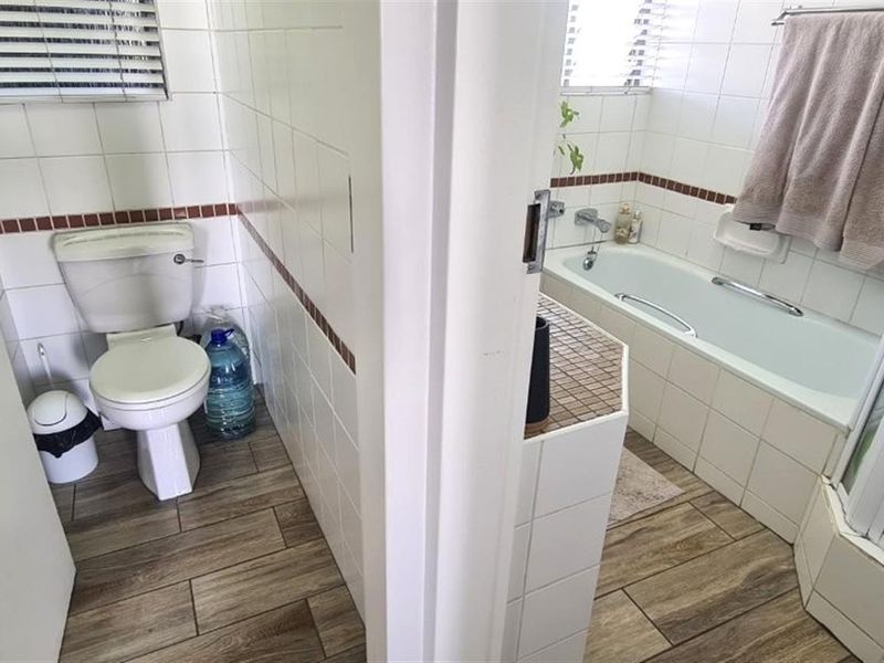 A functional bathroom featuring a separate toilet area, bathtub, and shower enclosure with tiled finishes and wood-look flooring.