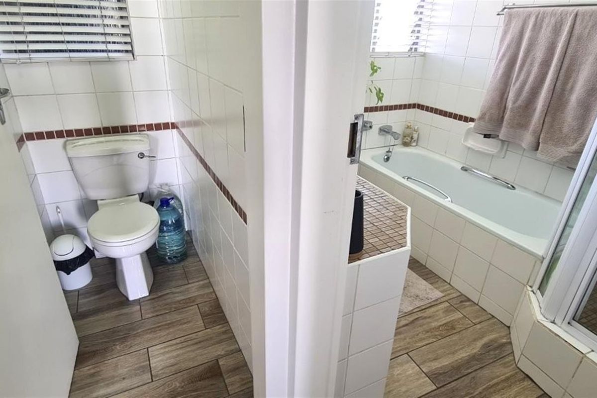 A functional bathroom featuring a separate toilet area, bathtub, and shower enclosure with tiled finishes and wood-look flooring.