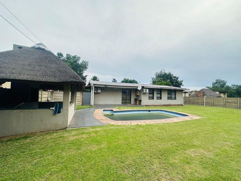 Rear exterior view featuring a swimming pool, a thatched lapa entertainment area, and a spacious lawn with perimeter walling.