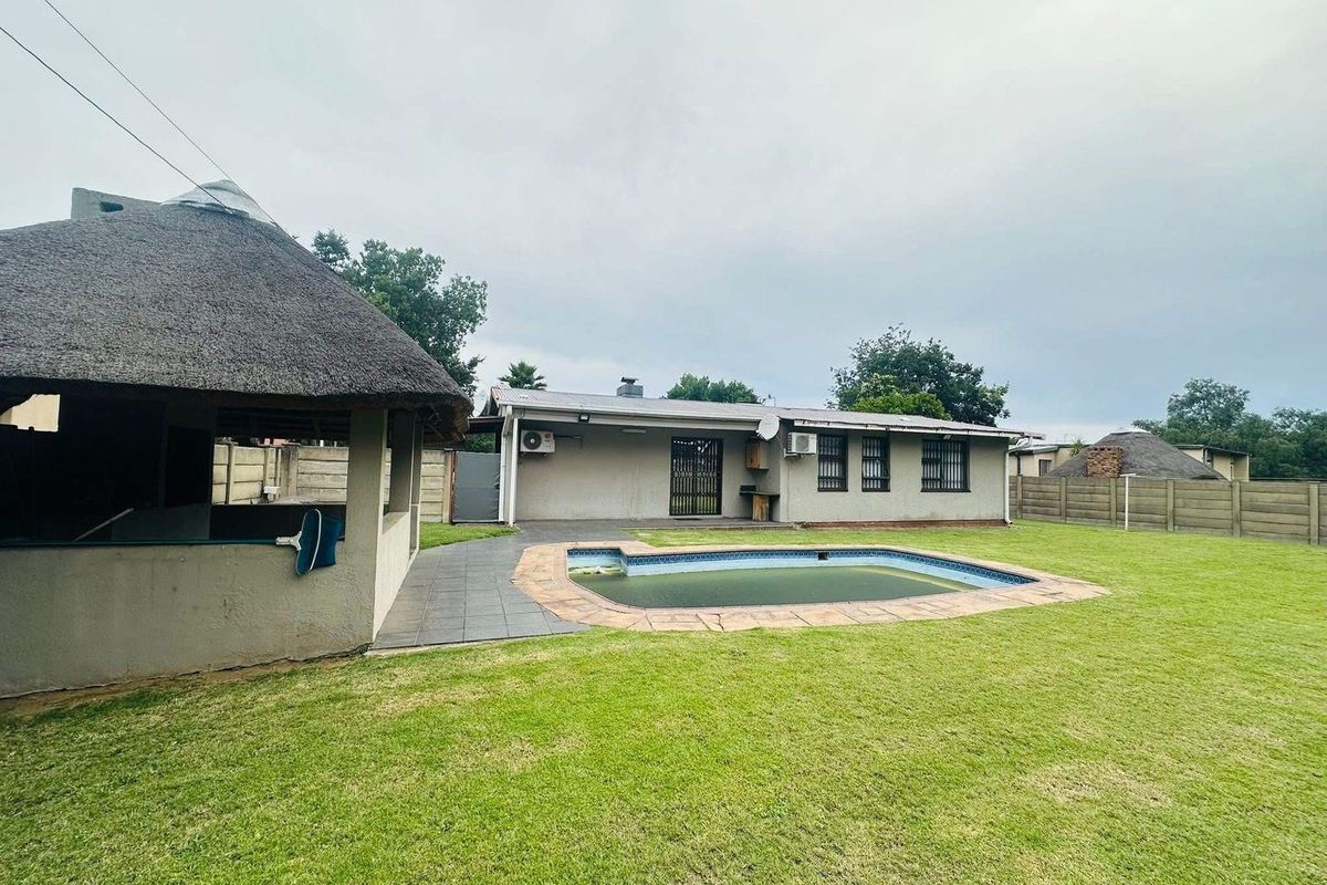 Rear exterior view featuring a swimming pool, a thatched lapa entertainment area, and a spacious lawn with perimeter walling.