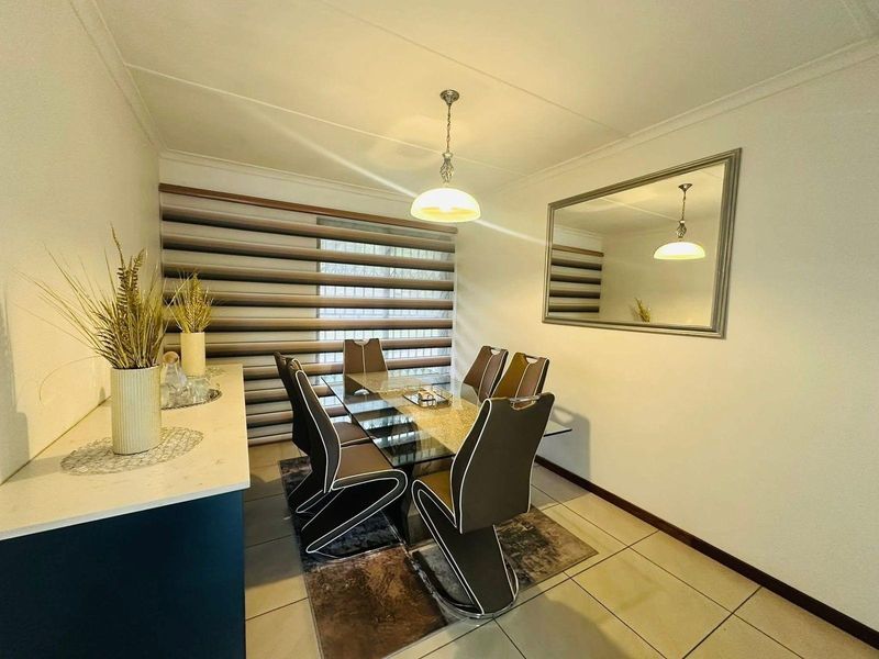 A well-maintained dining room featuring tiled flooring, modern window blinds, and a built-in serving counter with a stone-look countertop.