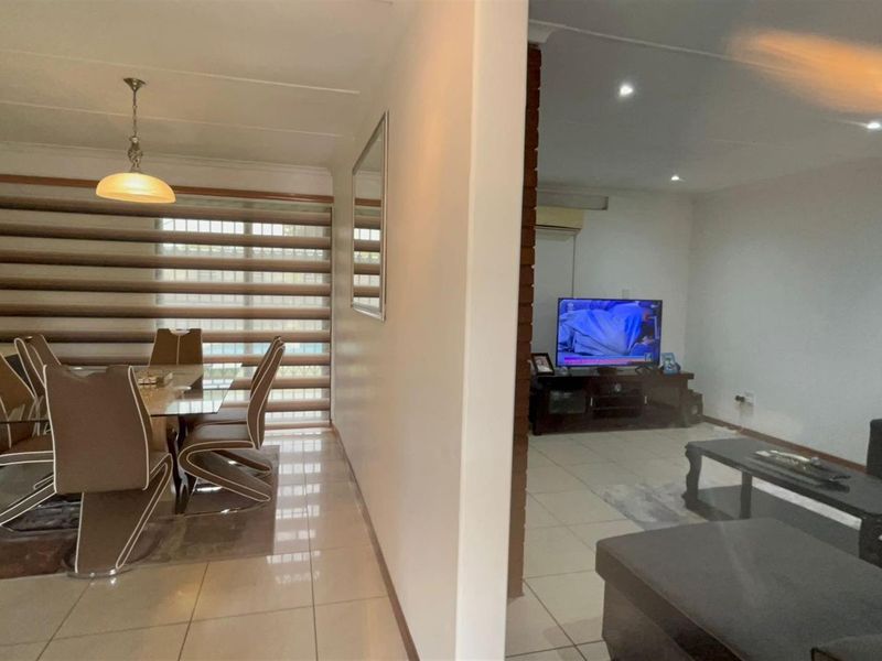 An open-plan living and dining area featuring tiled flooring, recessed ceiling lighting, and a brick feature wall separating the two spaces.
