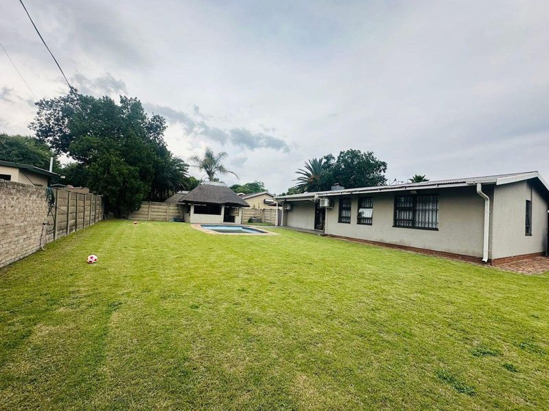 Spacious rear garden featuring a well-maintained lawn, a swimming pool, and a thatched lapa area, providing an ideal space for outdoor relaxation and entertainment.