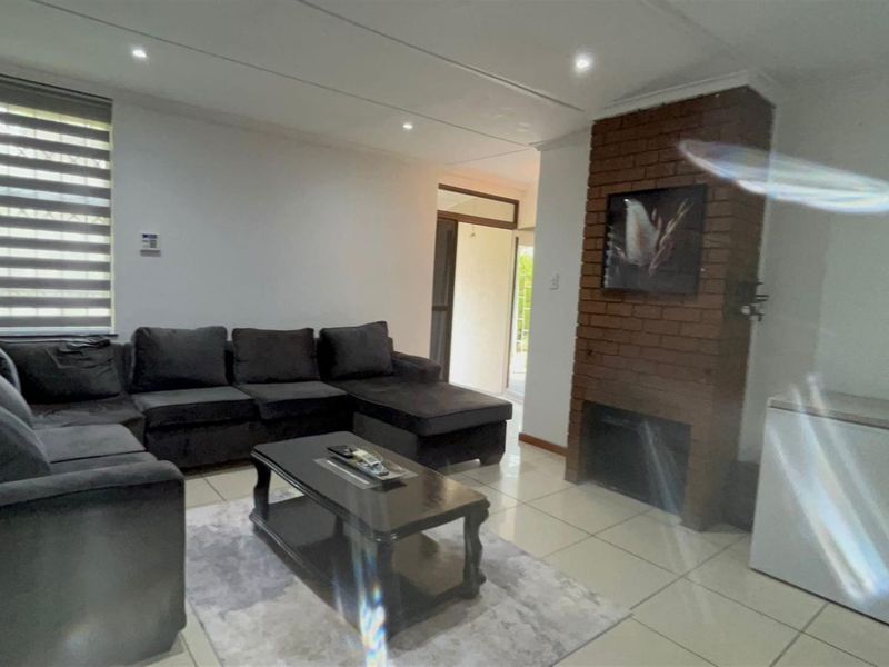 A living room featuring a prominent brick fireplace, tiled flooring, and recessed ceiling lighting, providing a functional and comfortable living space.