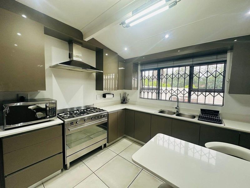 Modern kitchen featuring high-gloss cabinetry, stone countertops, a stainless steel gas range with extractor hood, and a double-basin sink.