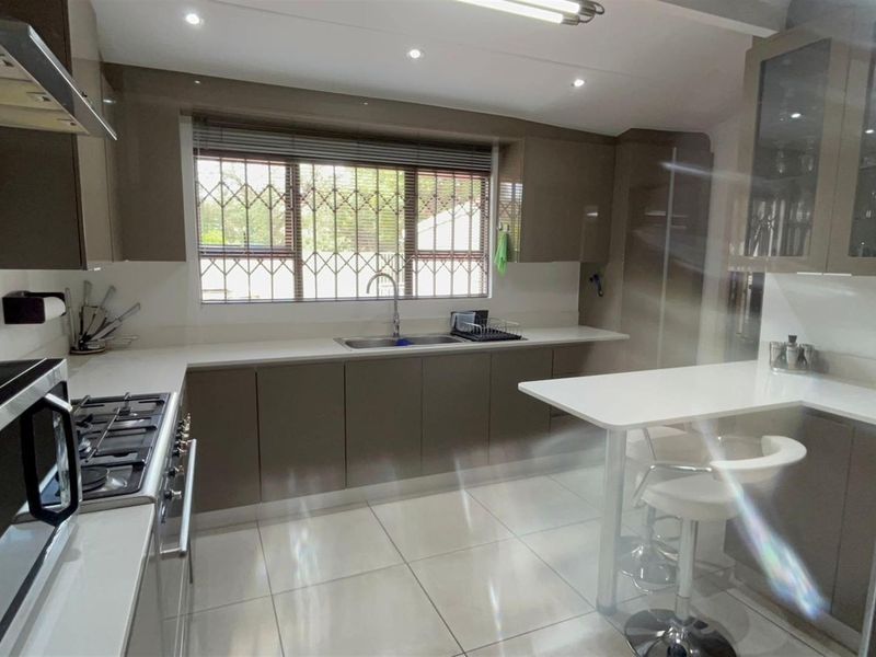Modern kitchen featuring sleek cabinetry, stone countertops, integrated gas hob, extractor fan, and a breakfast bar area with tiled flooring.