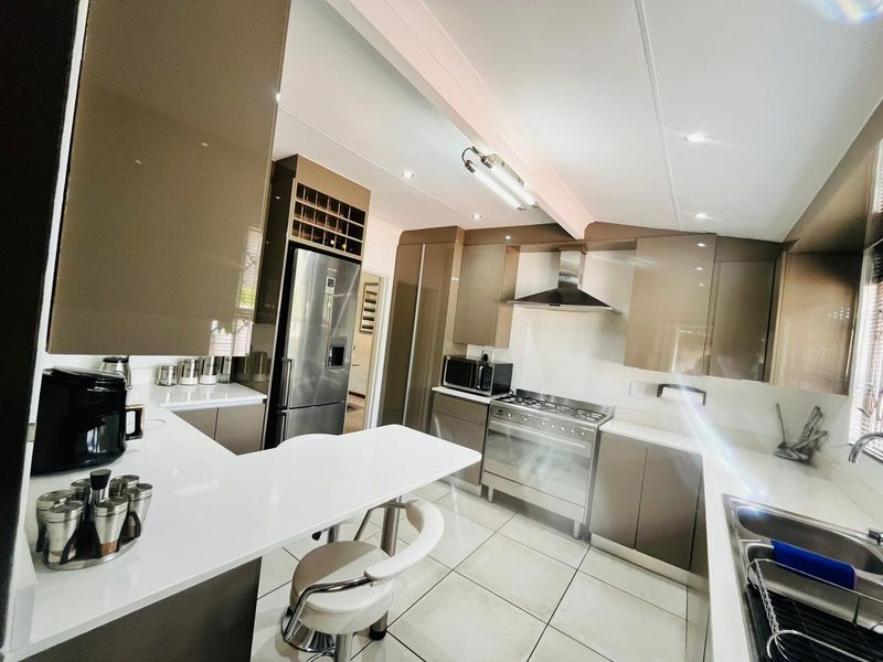 Modern kitchen featuring high-gloss cabinetry, stone countertops, stainless steel gas range with extractor hood, and integrated wine rack storage.