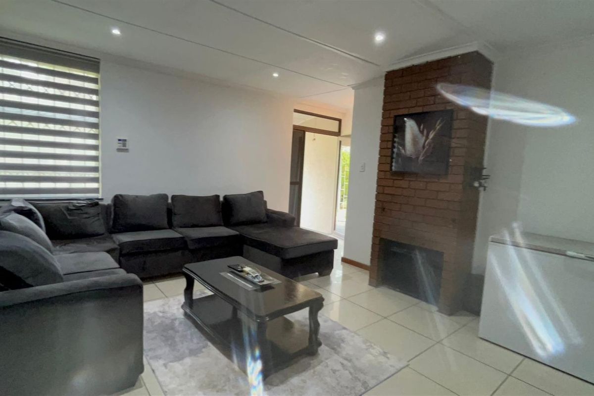 A living room featuring a prominent brick fireplace, tiled flooring, and recessed ceiling lighting, providing a functional and comfortable living space.