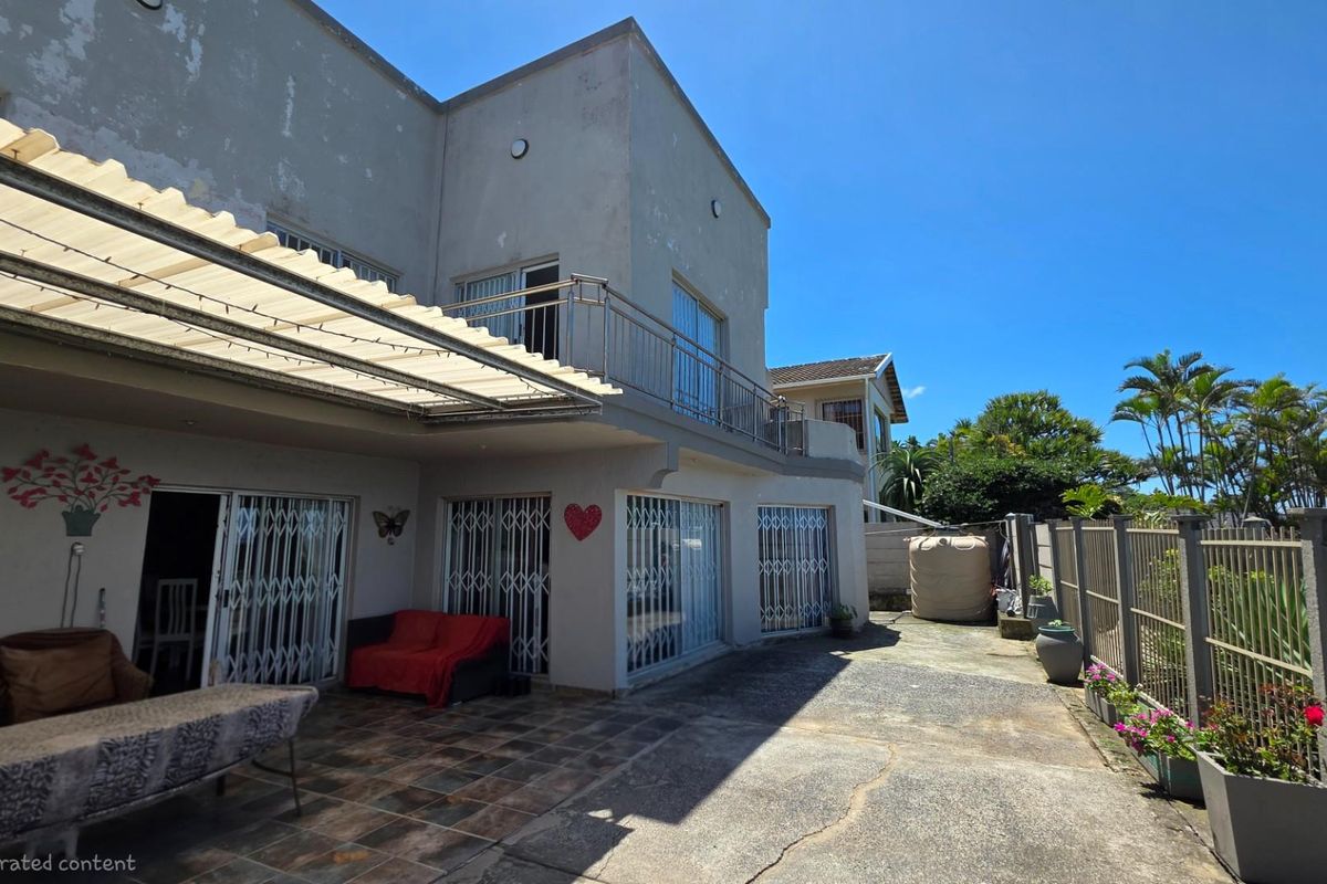 Rear exterior view of a multi-story house featuring a covered patio area, tiled flooring, metal security gates, and a balcony with stainless steel railings.