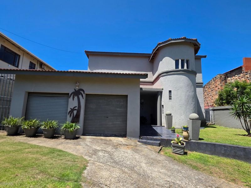 Front exterior view of a two-story house featuring a double garage, a distinctive curved architectural tower, and a paved driveway with surrounding lawn.