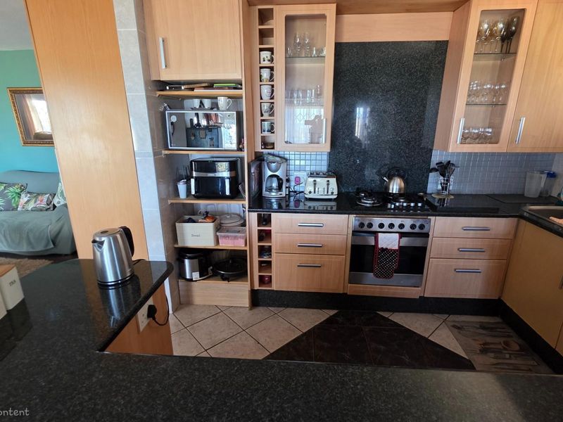 A functional kitchen featuring light wood cabinetry, dark granite countertops, a built-in oven, gas hob, and an integrated extractor fan.