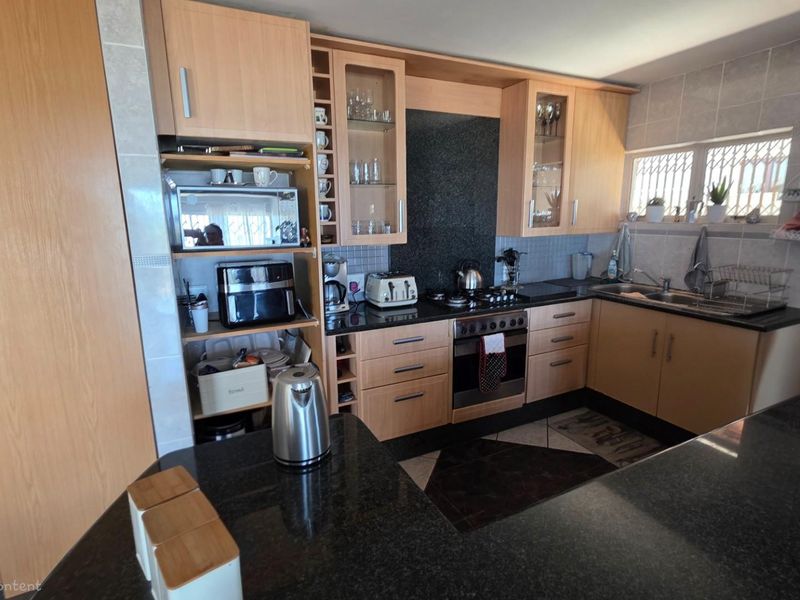 A functional kitchen featuring light wood cabinetry, dark granite countertops, a built-in oven with gas hob, and tiled splashbacks.