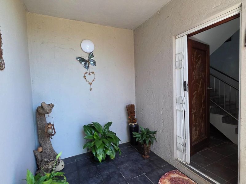 A covered entrance porch featuring dark tiled flooring and a security gate leading into the main residence.