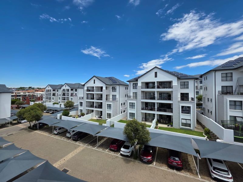 Exterior view of a modern apartment complex featuring multi-story buildings with balconies, solar panels, and dedicated covered parking bays.