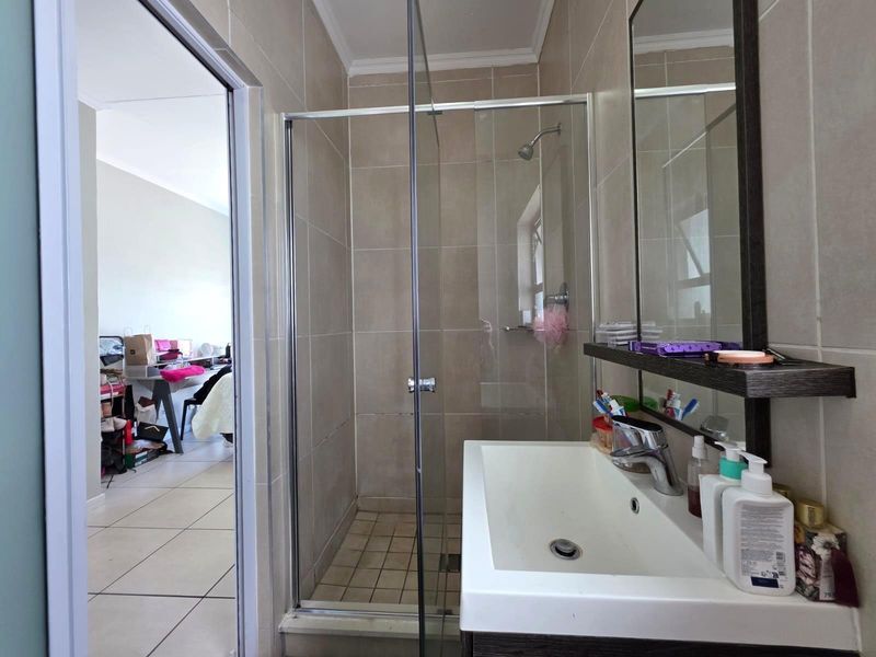 A functional bathroom featuring a glass-enclosed shower, wall-mounted vanity basin with mixer tap, and neutral wall tiling.