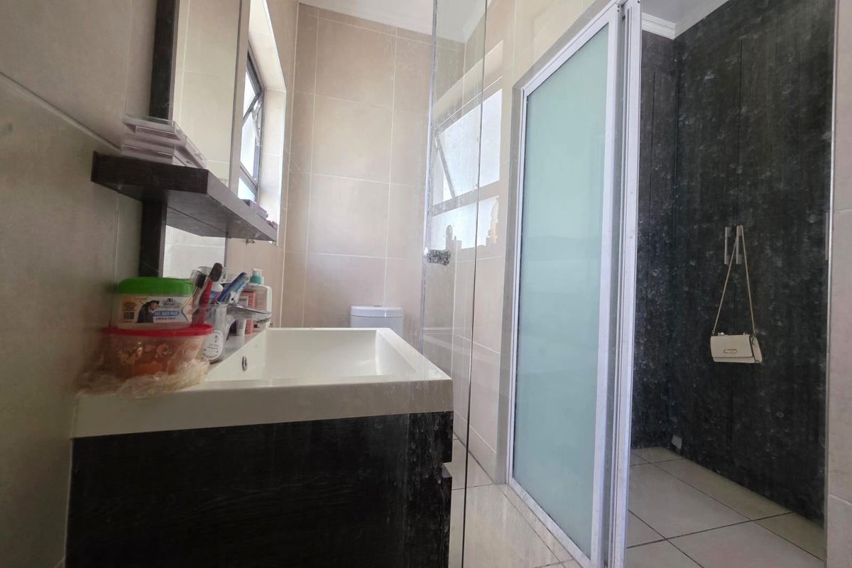 Modern bathroom featuring a vanity with basin, a glass-enclosed shower with sliding door, and neutral wall and floor tiling.