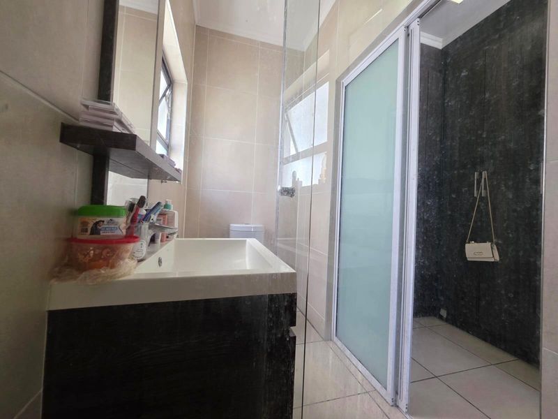 Modern bathroom featuring a vanity with basin, a glass-enclosed shower with sliding door, and neutral wall and floor tiling.