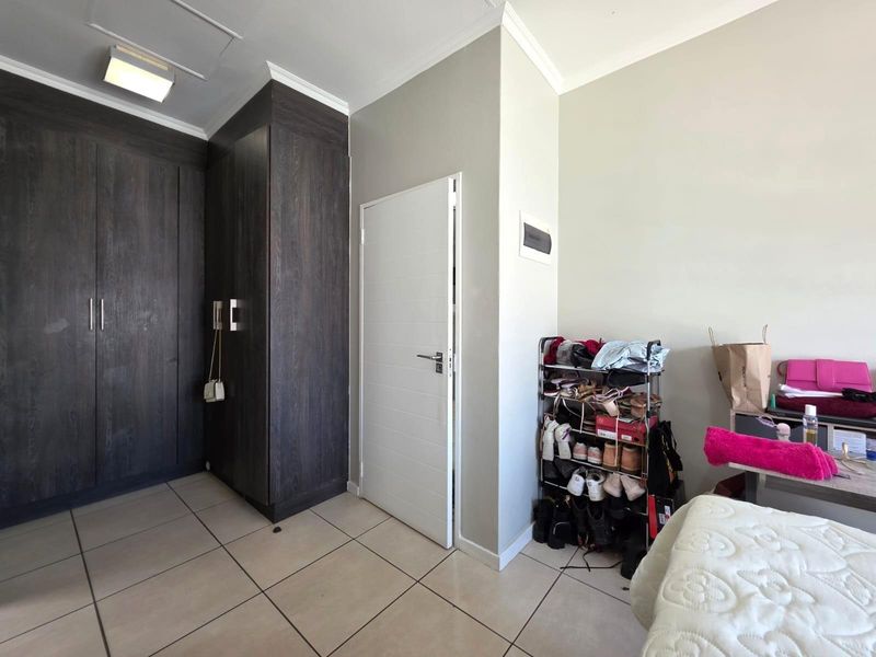 A bedroom featuring dark wood built-in cupboards, neutral tiled flooring, and a clean, modern interior finish.