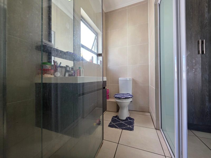 A functional bathroom featuring a glass-enclosed shower, vanity cabinet, and neutral wall tiling.