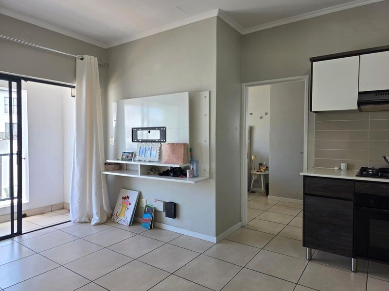 Open-plan living area featuring tiled floors, a built-in media unit, and a modern kitchen with integrated appliances, leading to a private balcony.