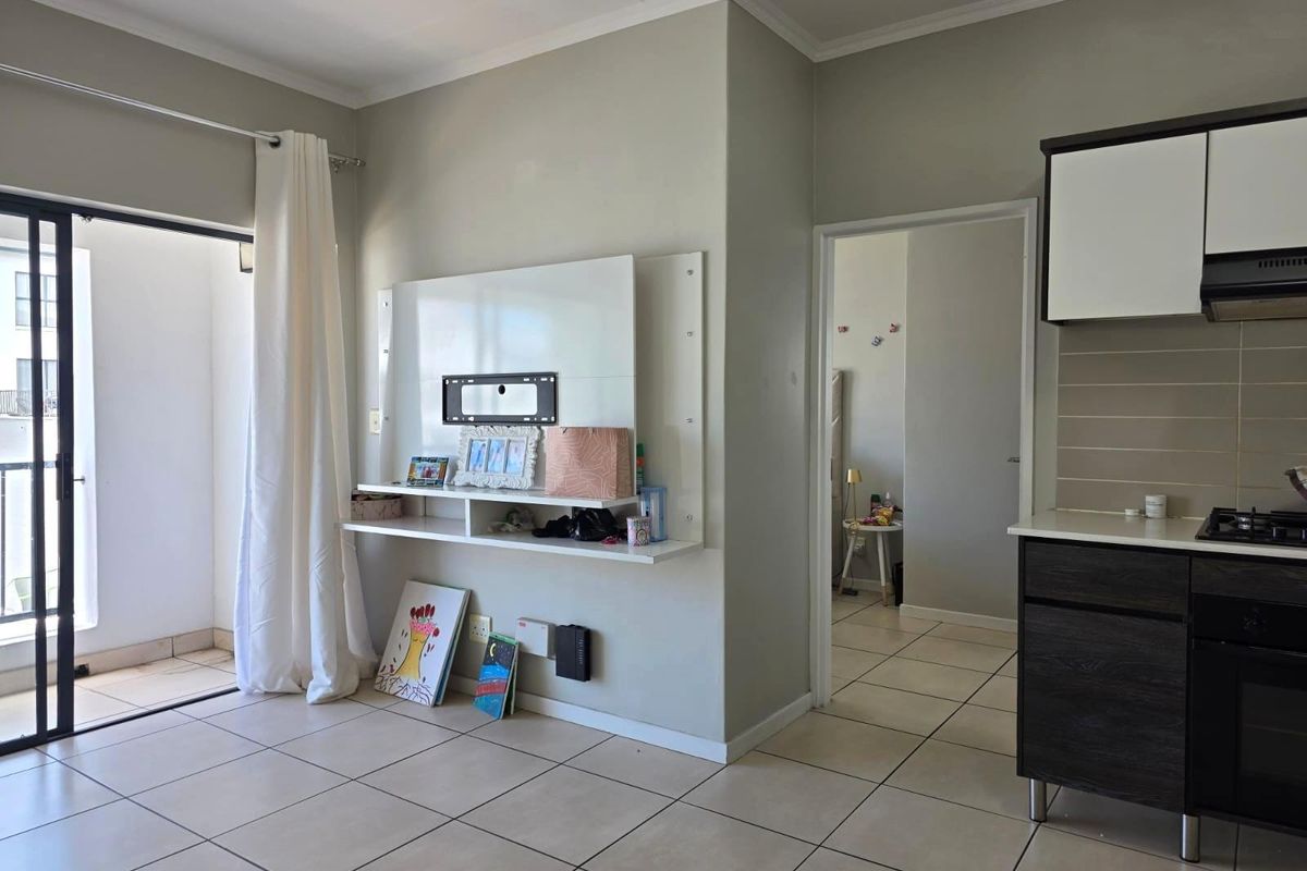 Open-plan living area featuring tiled floors, a built-in media unit, and a modern kitchen with integrated appliances, leading to a private balcony.