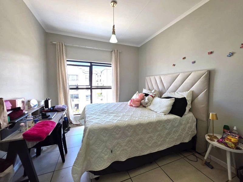 A well-lit bedroom featuring tiled flooring, a large window providing natural light, and a neutral color palette.