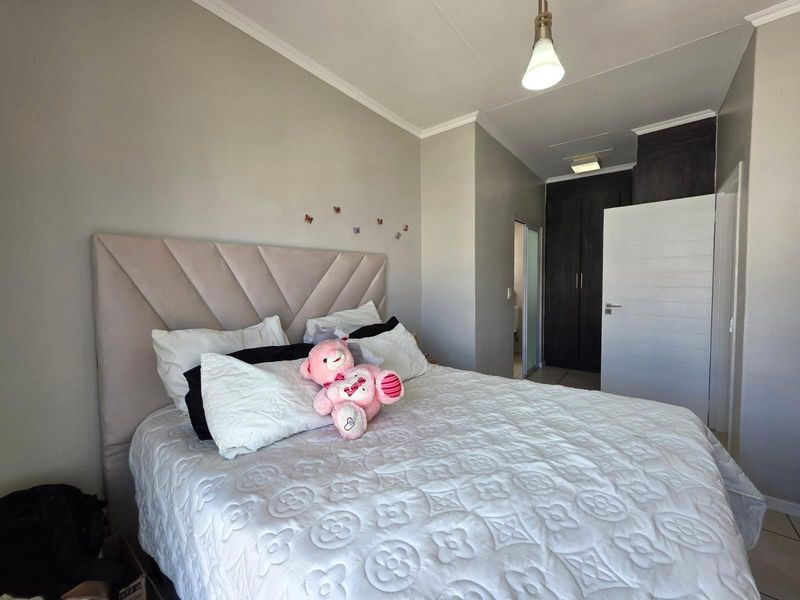 A well-maintained bedroom featuring built-in cupboards, neutral wall finishes, tiled flooring, and a modern pendant light fixture.