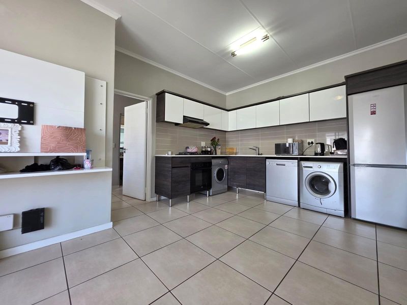 A functional kitchen featuring modern two-tone cabinetry, tiled backsplash, built-in oven, extractor fan, and integrated space for laundry appliances.