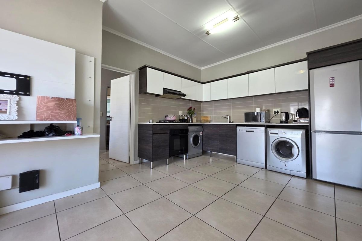 A functional kitchen featuring modern two-tone cabinetry, tiled backsplash, built-in oven, extractor fan, and integrated space for laundry appliances.