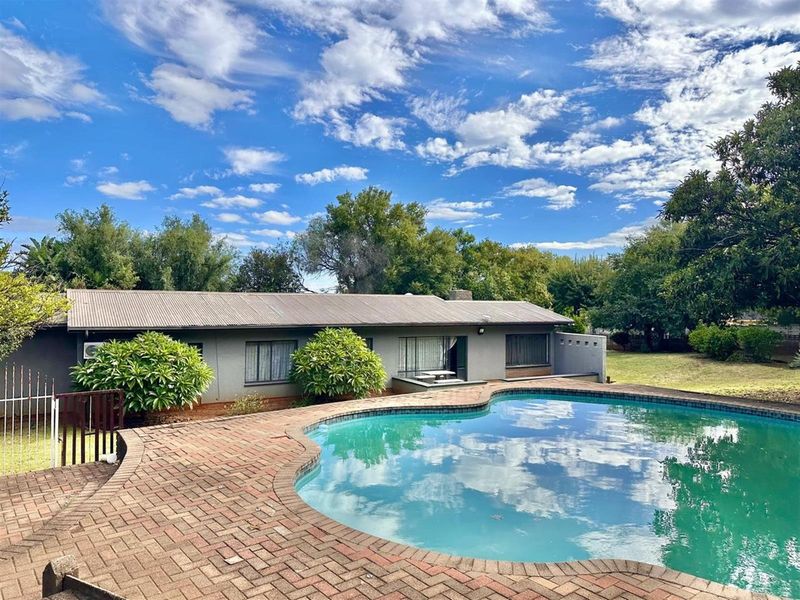 Rear view of the property featuring a swimming pool with brick paved surround and a spacious garden area.